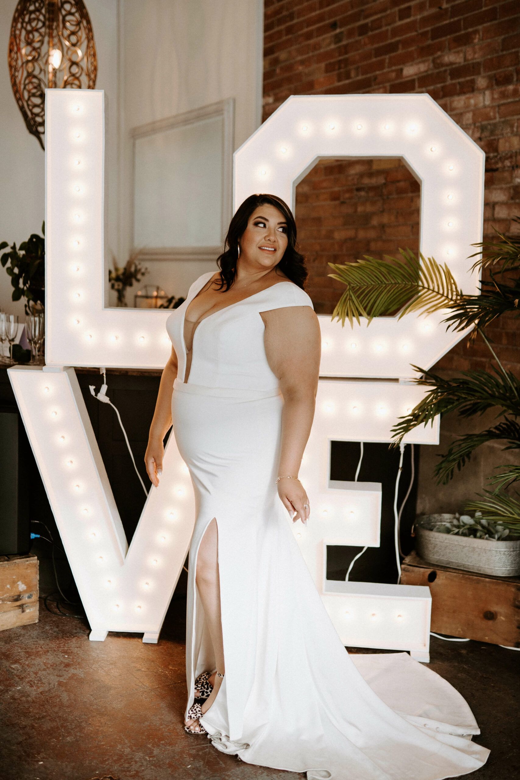 A woman in a white dress is standing in front of a large love sign.