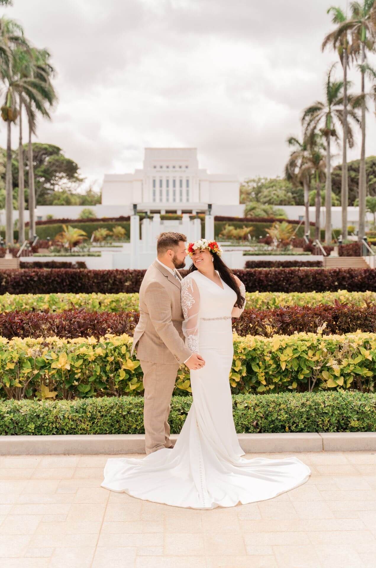 A bride and groom are kissing in front of a temple.