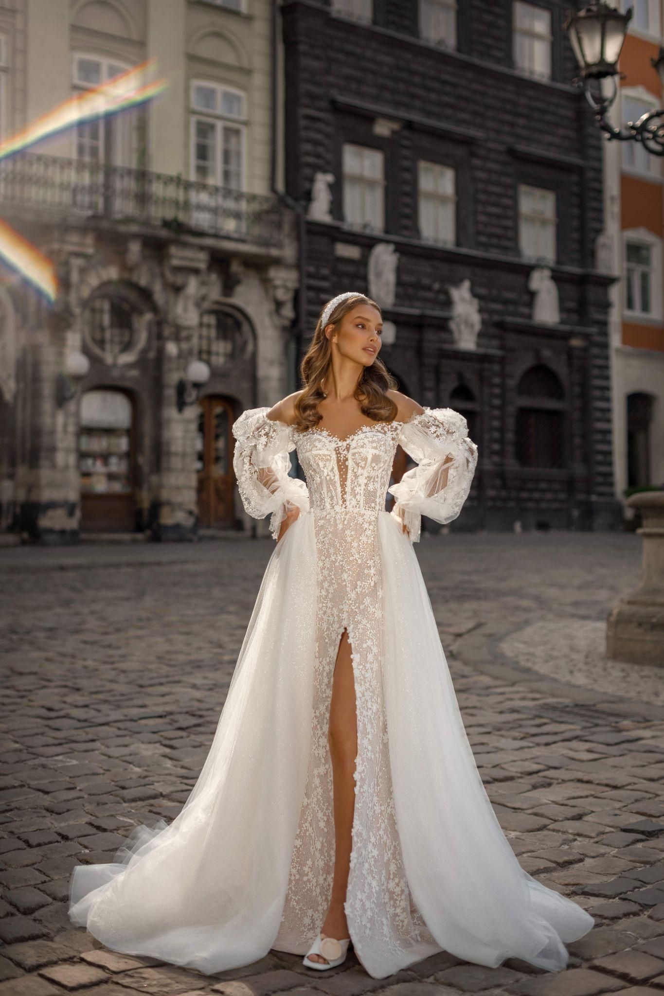 A woman in a white wedding dress is standing on a cobblestone street in front of a building.
