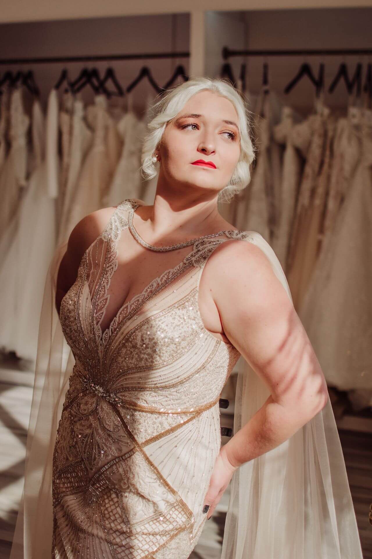 A woman in a wedding dress is standing in front of a row of wedding dresses.