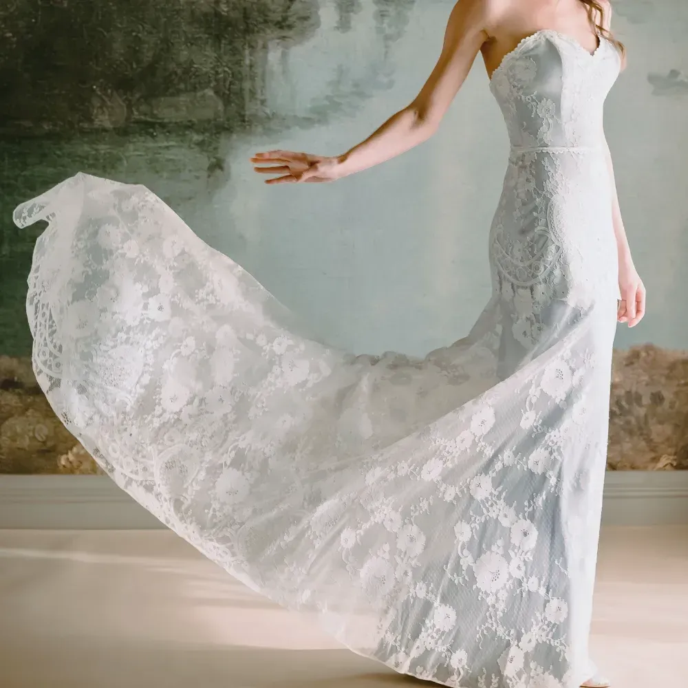 A woman in a white lace dress is standing in front of a painting