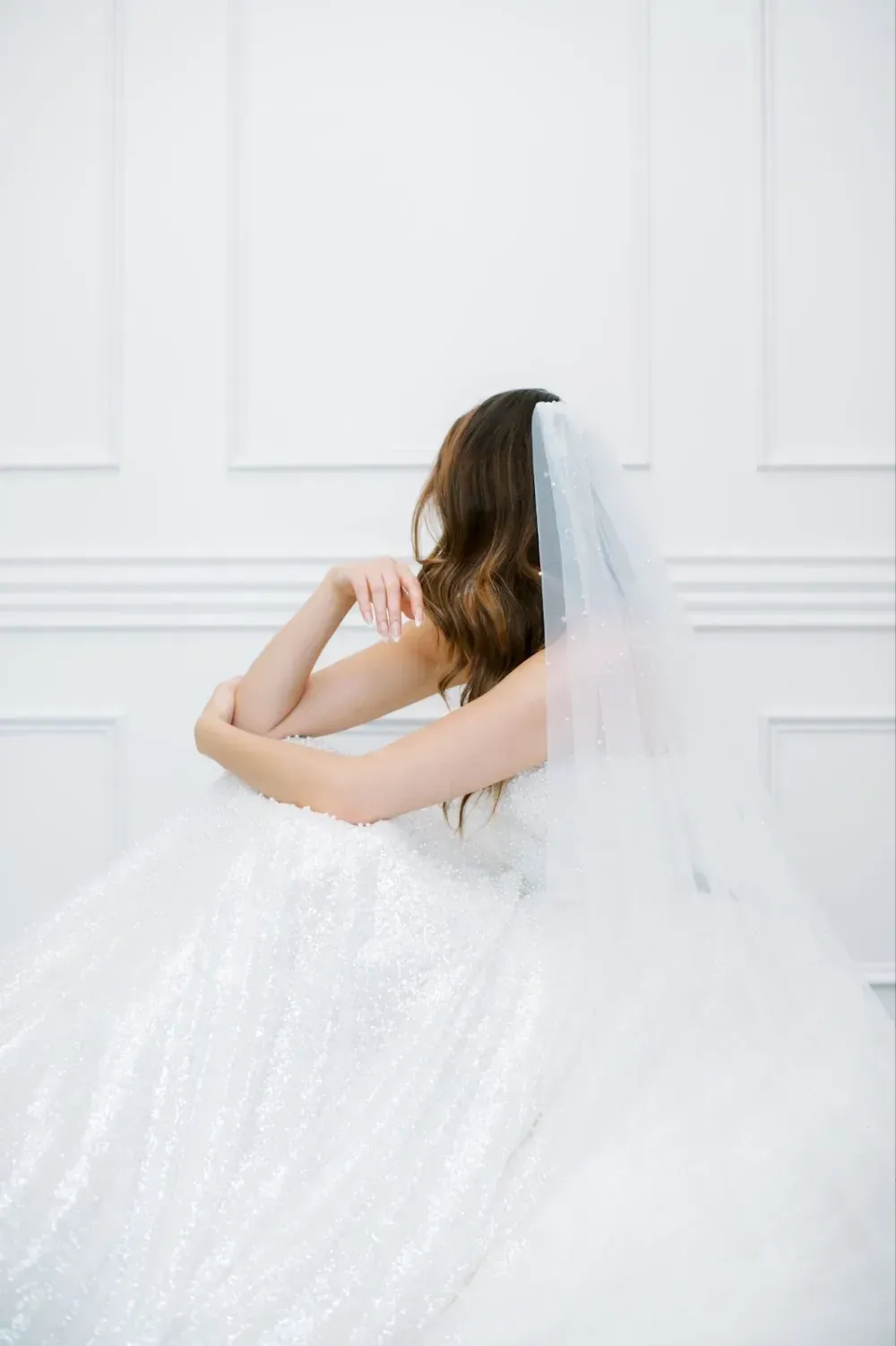 A bride in a wedding dress and veil is sitting on a bed.
