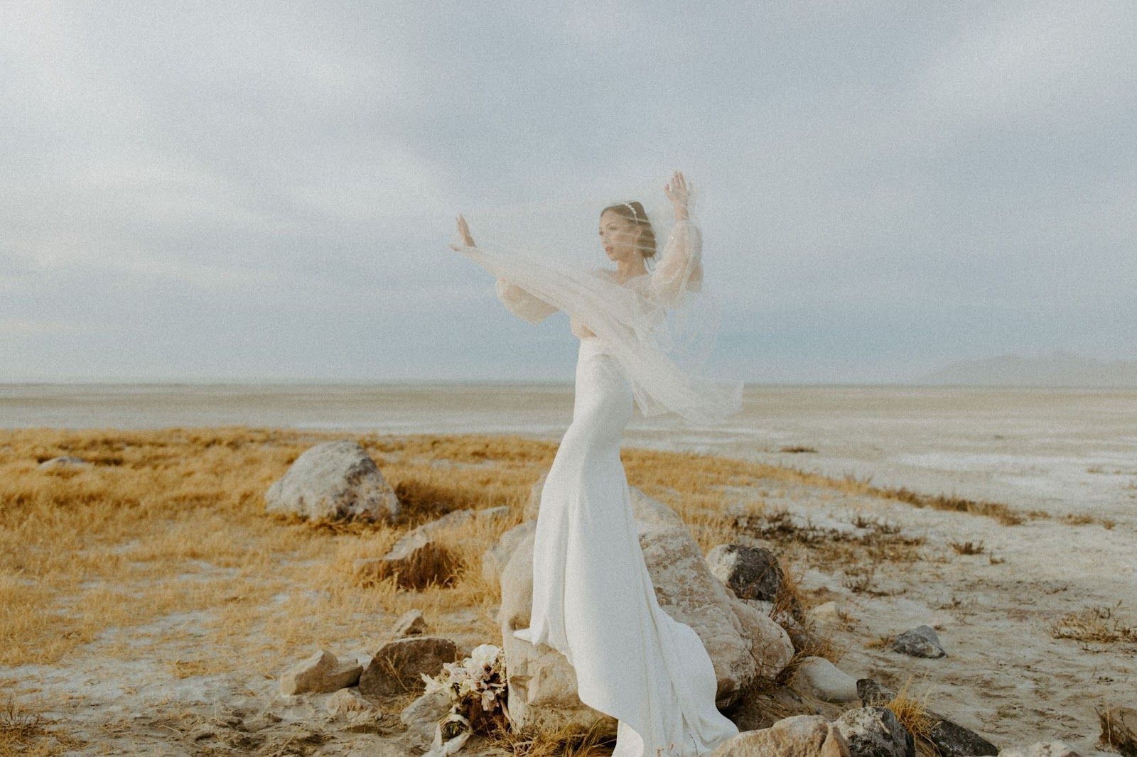 A woman in a white dress is standing on a rock in the desert.