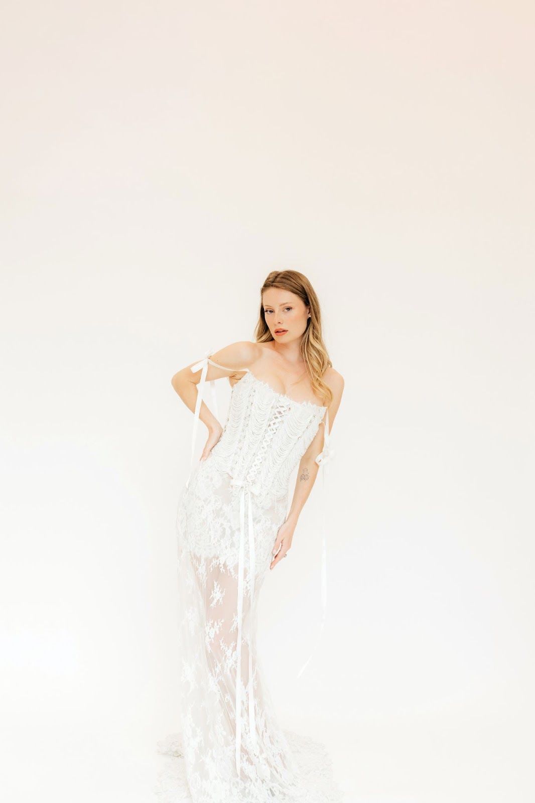 A woman in a white dress is standing in front of a white wall.