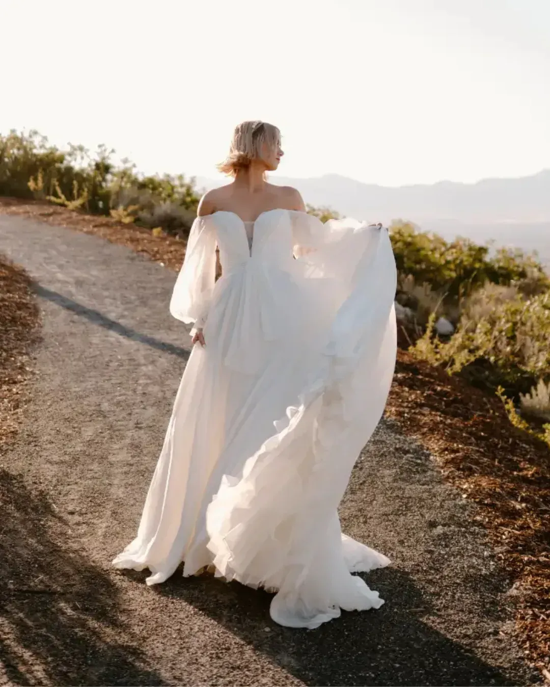 A woman in a white dress is walking down a dirt road.