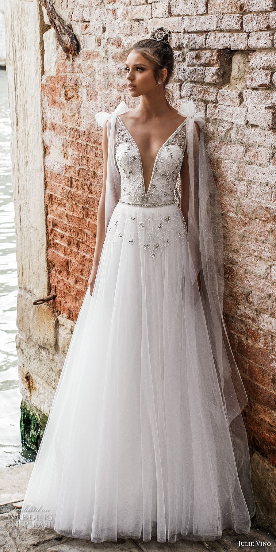 A woman in a white wedding dress is standing in front of a brick wall.
