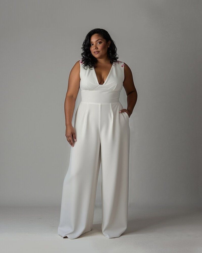 Woman wearing a white sleeveless jumpsuit with wide legs, posing against a gray backdrop.