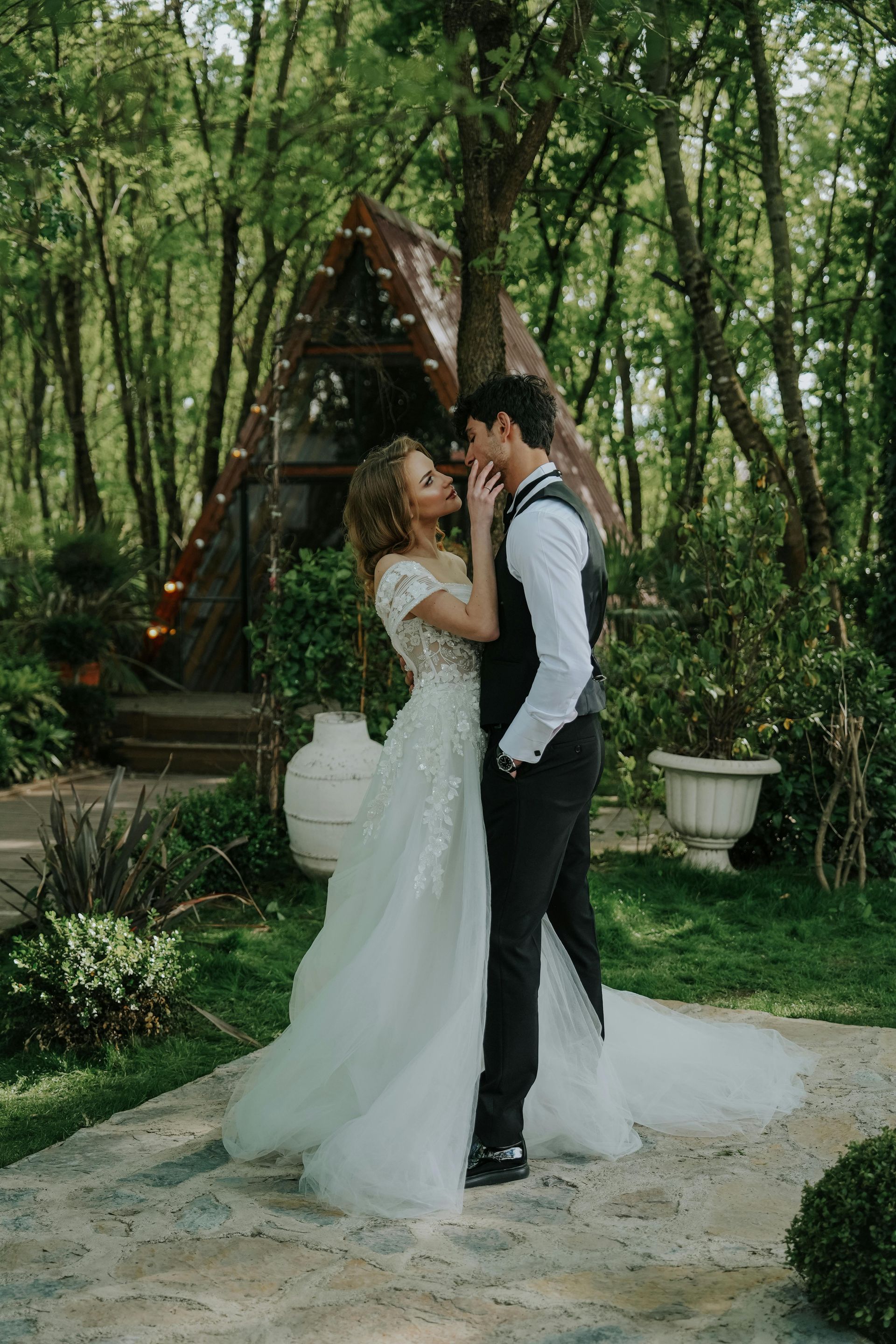 A bride and groom are kissing in front of a cabin in the woods.