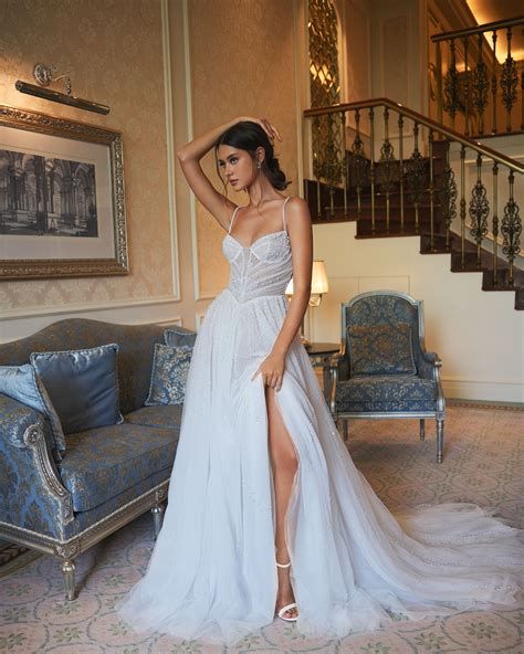 Woman in white wedding dress with high slit, posing in elegant room with staircase.