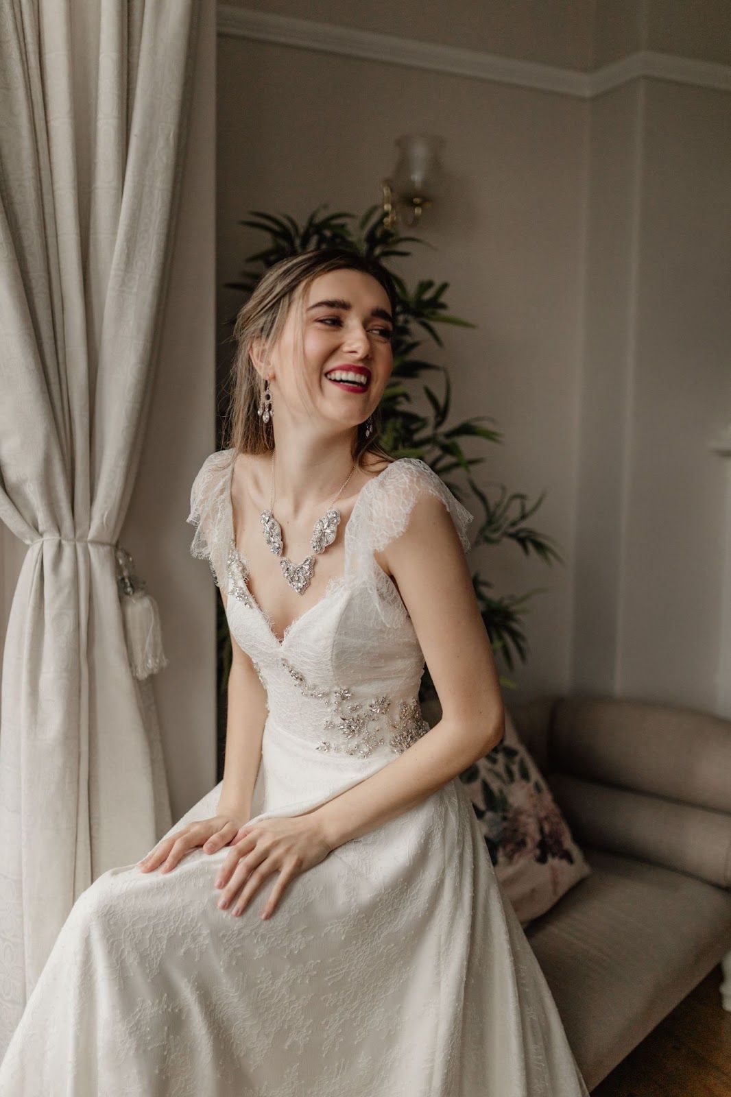 A woman in a wedding dress is sitting on a couch and smiling.