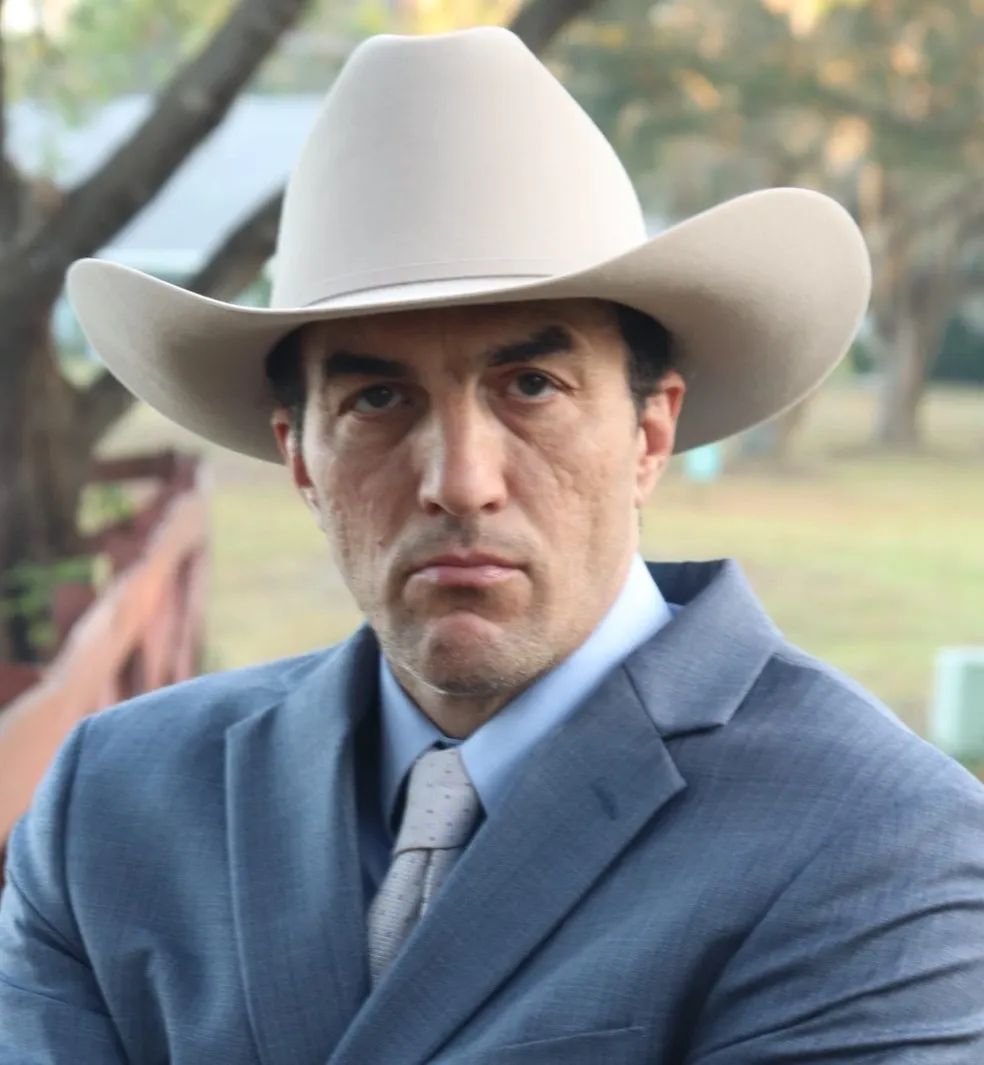 Man in cowboy hat and suit, outdoors with a serious expression.