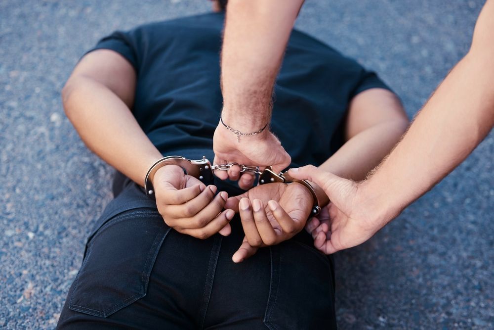 Person lying face down on pavement, being handcuffed.