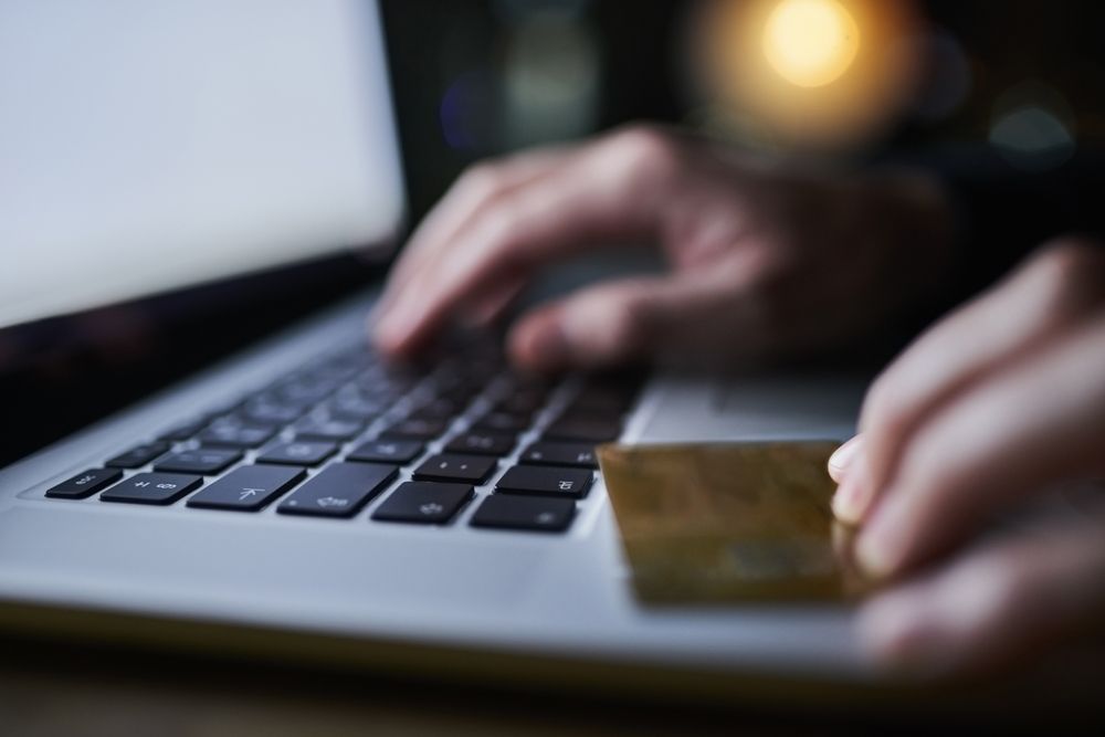 Hands typing on laptop keyboard, holding a gold credit card.