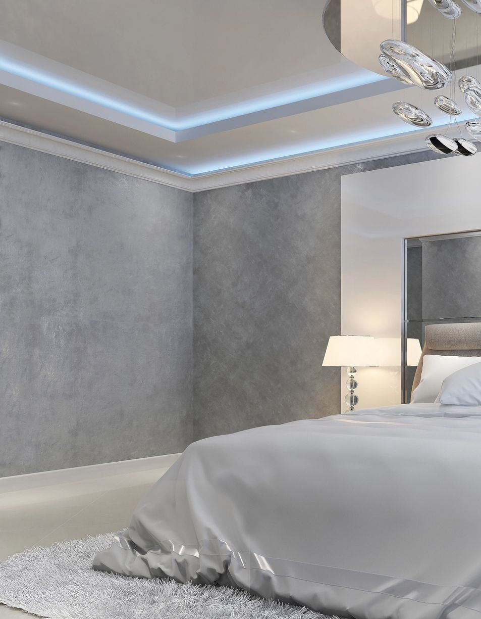 Camera da letto grigia e bianca con letto, lampada, pareti strutturate e luci al soffitto.