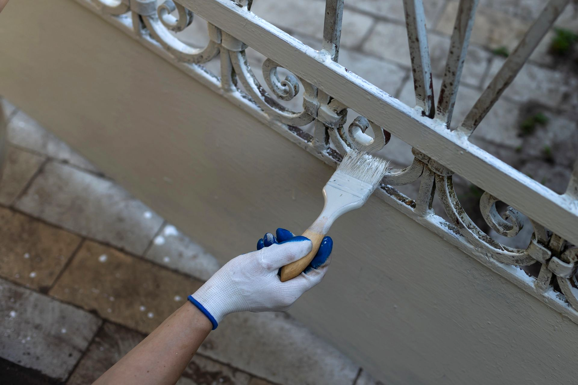Persona che indossa guanti mentre dipinge una ringhiera in ferro battuto bianco con un pennello.