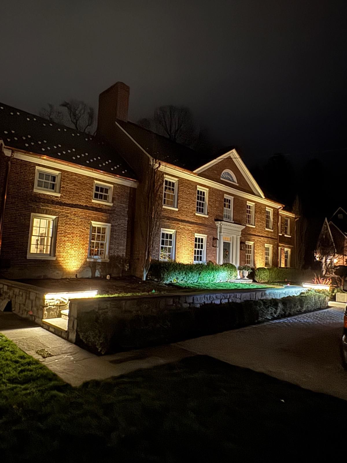 Brick building illuminated at night with white trim and a small front garden.