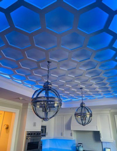 Honeycomb ceiling with blue LED lighting, two pendant lights, and white kitchen cabinets.