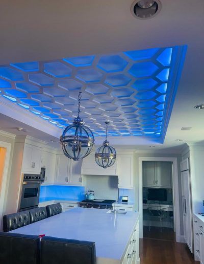 Kitchen ceiling with honeycomb design and blue lighting, two pendant lights over a white island.