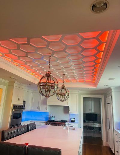 Kitchen ceiling with honeycomb design illuminated by orange lights, with two globe pendant lights hanging below.