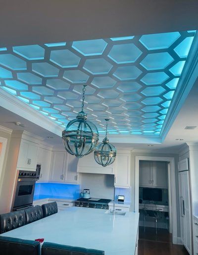 Honeycomb-patterned ceiling with blue backlighting in a modern kitchen, accented by globe pendant lights.