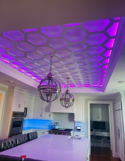 Kitchen with a hexagon-patterned ceiling lit with purple lights, pendant lights, and a white island.