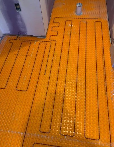 Orange heated floor mat installed in a bathroom, ready for tile.