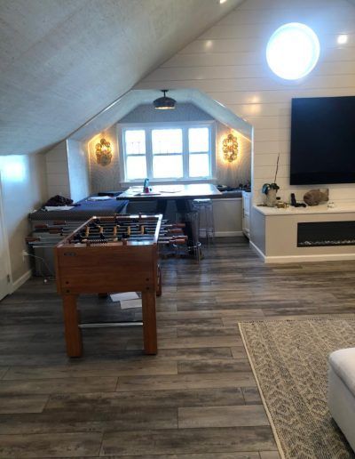 Foosball table in a bright, modern game room with a large screen TV, desk, and a round window.