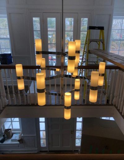 Modern chandelier hanging in a two-story entryway, with two glass doors and natural light.
