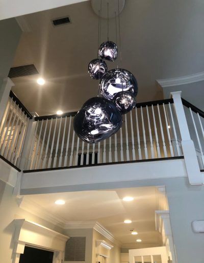 Modern chandelier with reflective orbs hangs from a high ceiling, visible above a white and black balcony.