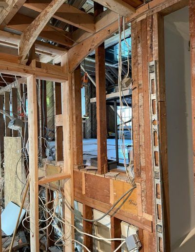 Interior of a building under renovation, showing exposed wooden framing, electrical wires, and partial walls.