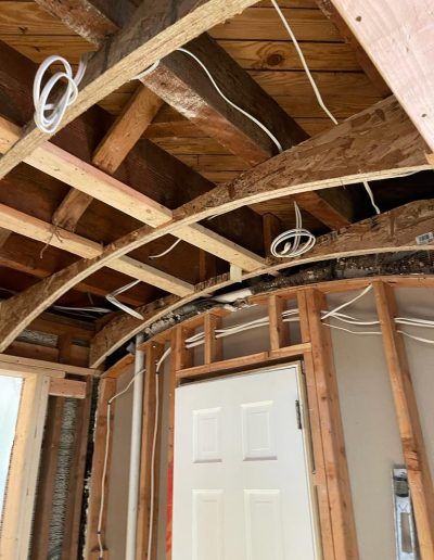 Interior view during renovation, exposing curved wooden ceiling beams and electrical wiring. White door visible.