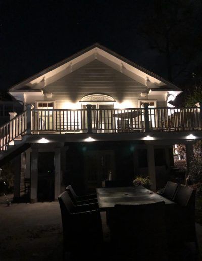 Lit-up house at night with a deck. Patio furniture is in the foreground.