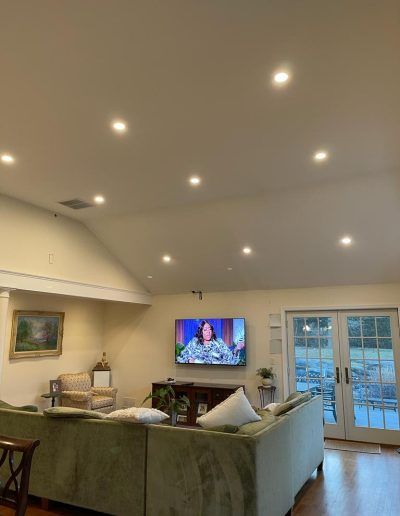 Living room with green sofa, TV on wall, and recessed ceiling lights. French doors lead outside.