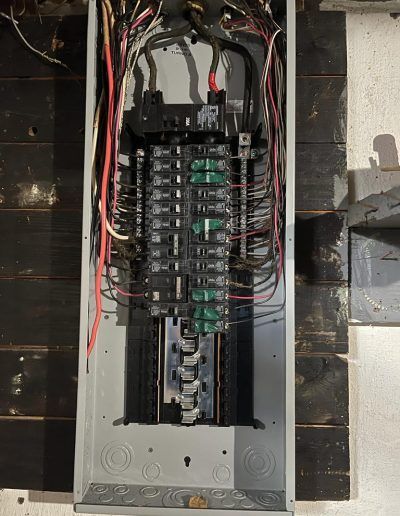 Electrical panel with circuit breakers and wiring. Gray panel on a dark wood wall.