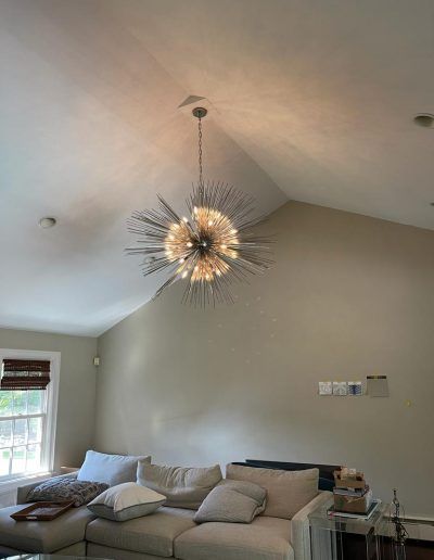 A large sputnik chandelier hangs from a high, sloped ceiling in a living room with a beige couch.