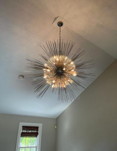 A large, spiky, round chandelier hangs from a high, slanted ceiling in a room.