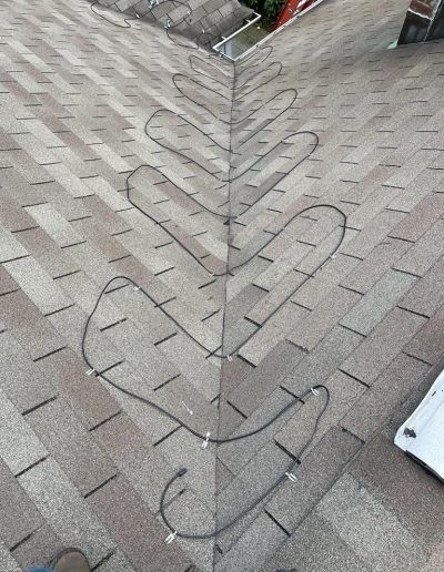Close-up of a roof corner with black heat cable zig-zagging along the shingles to prevent ice dams.