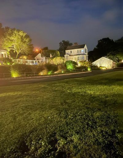 Night view of a two-story house, lit with warm landscape lighting, set against a dark sky.