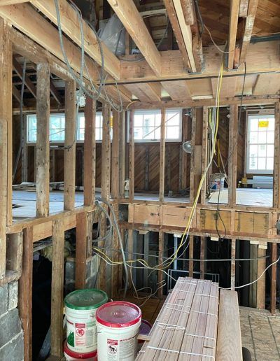 Interior home under construction, exposed wooden framing, visible wiring, buckets, and stacked lumber.