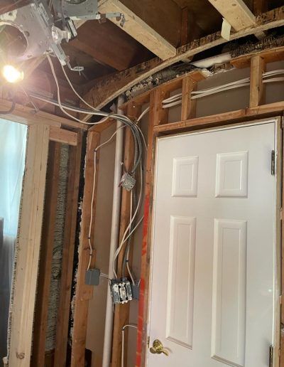 Interior construction view of a room with exposed framing, wiring, and a white door.