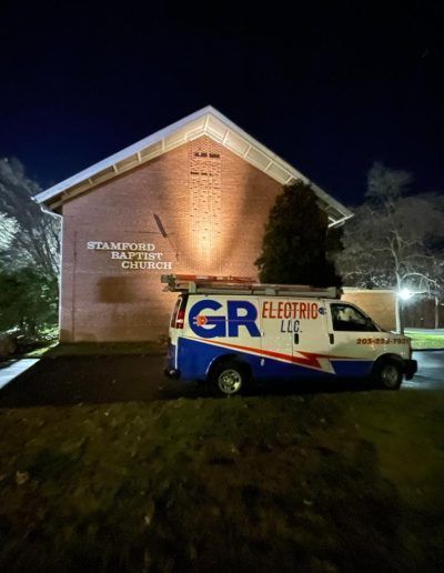 A van from GR Electric LLC parked in front of Stamford Baptist Church at night.