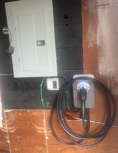 Electrical panel and EV charger mounted on a wall. Black cord coiled.