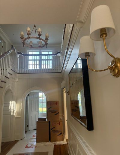 An entryway with a staircase, chandelier, and a mirror, with moving boxes on the floor.