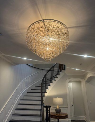Large, woven chandelier above a curved staircase with black railing and dark treads.