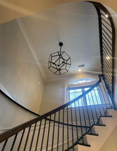 Staircase with dark wood banister and a geometric chandelier. Light streams through a window.
