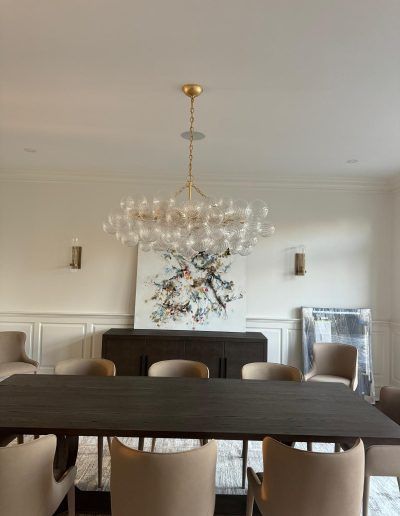 Dining room with chandelier over dark wood table, chairs, and artwork.