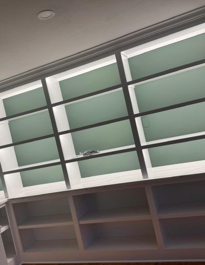 Built-in white shelving unit with open lower shelves and upper cabinets with light green interiors.