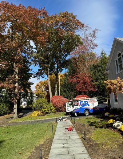 A blue and white GR Utility truck parked on a driveway with trees and fall foliage, sunny day.