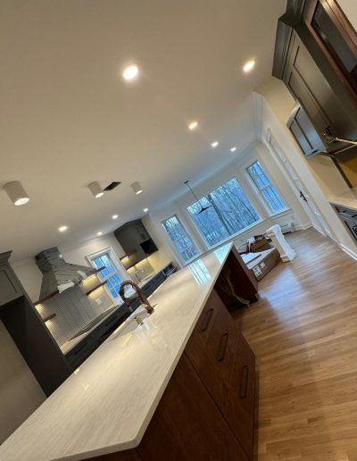 Modern kitchen with white countertops, wooden cabinets, and large windows.