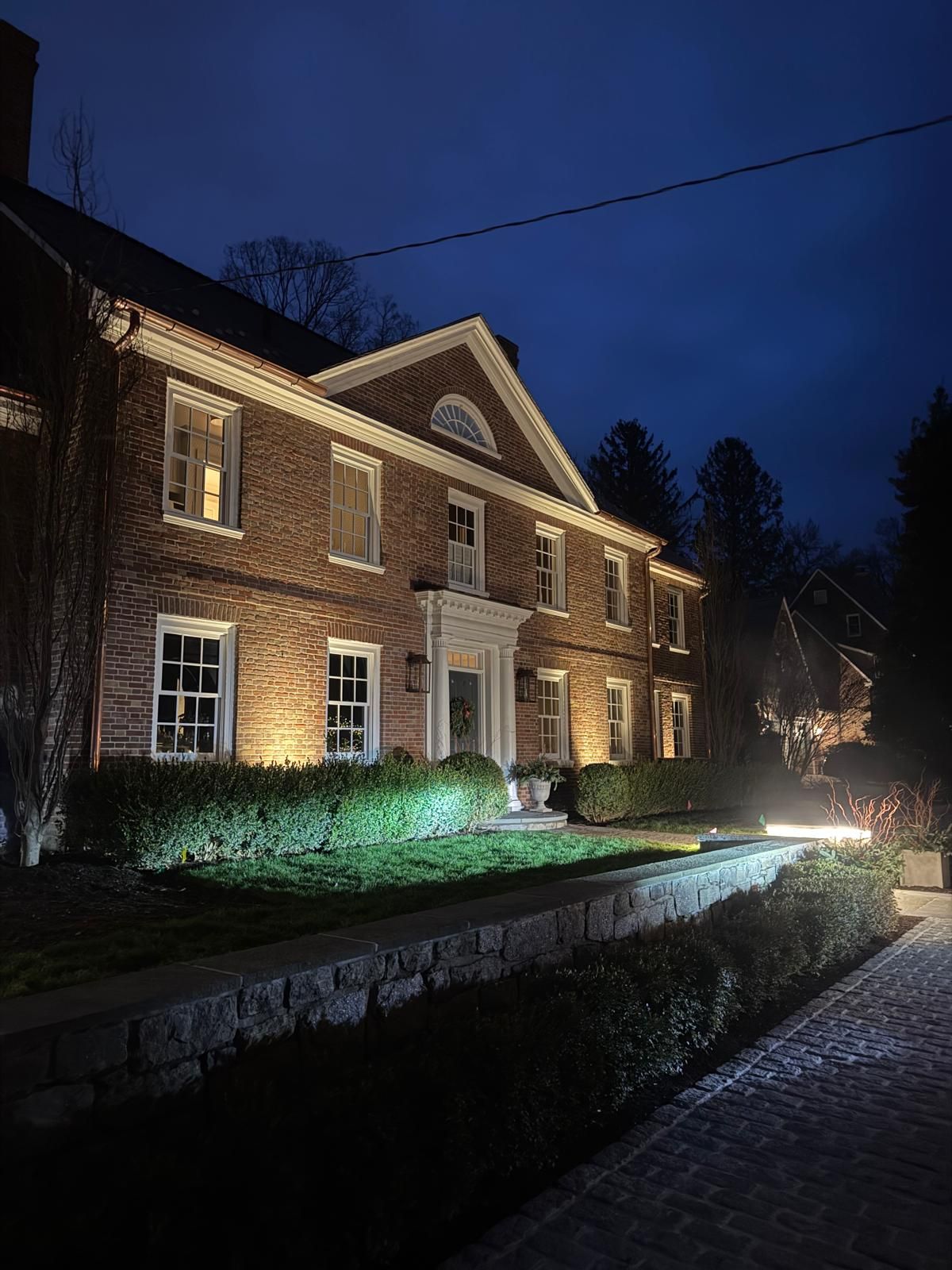 Brick house illuminated at night with garden lighting and a dark blue sky.